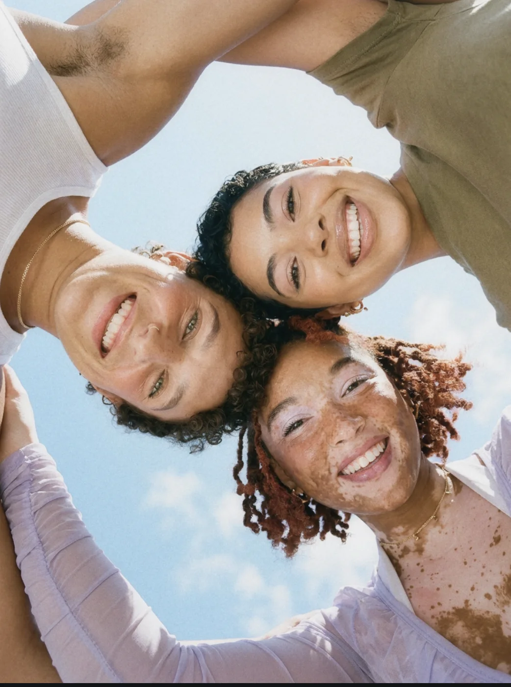 Three friends laughing together, photographed from below against a blue sky